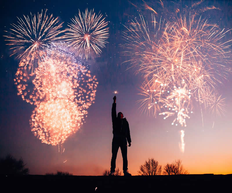 Silhouette of man standing in front of fireworks.
